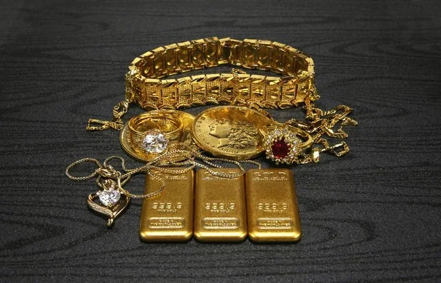 金の指輪とネックレス、金貨を木製の台に並べた写真